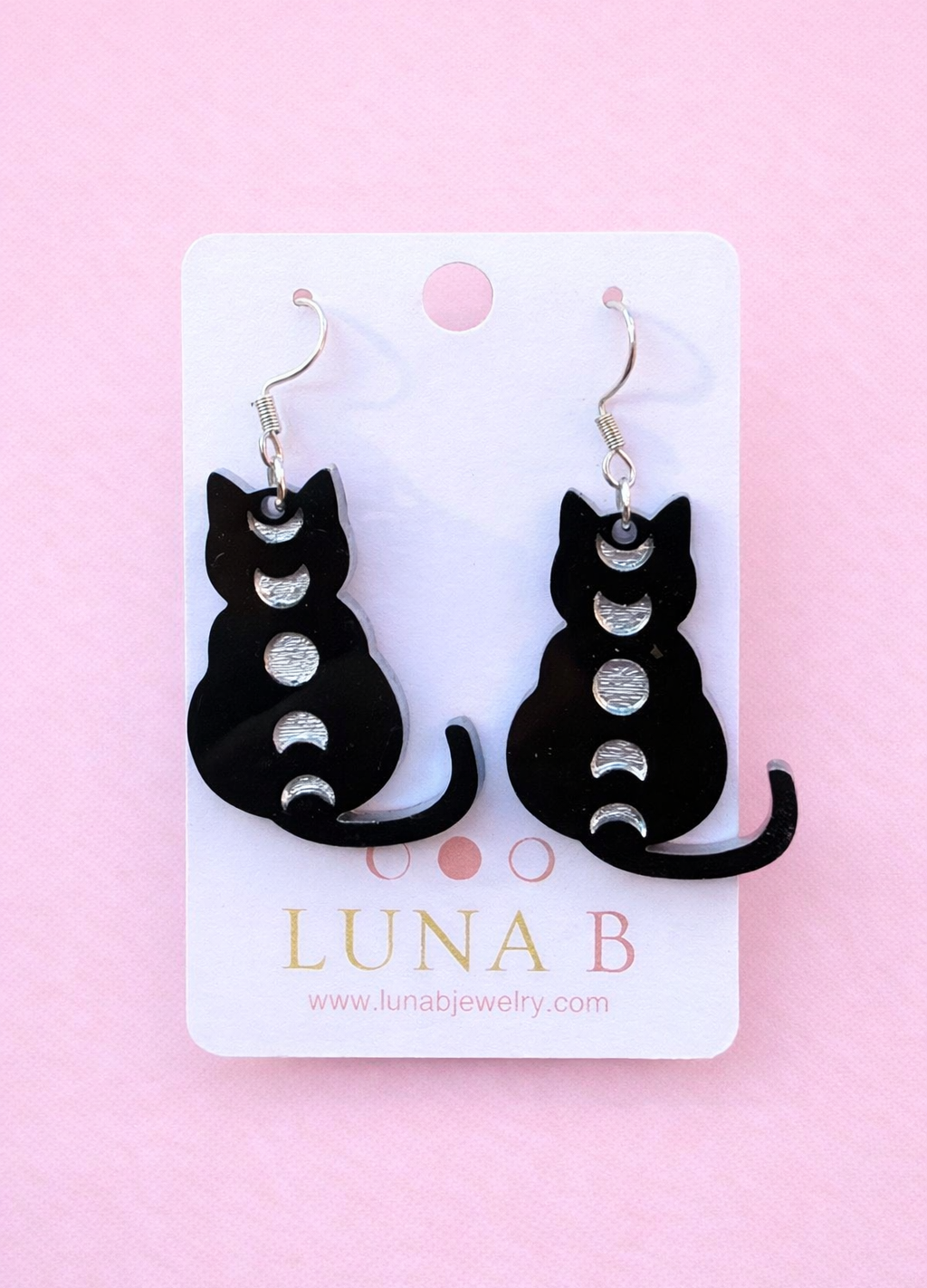Black cat-shaped earrings on a Luna B branded card against a pink background