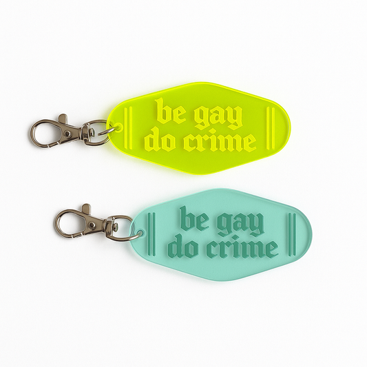 Laser-cut acrylic motel keychains in neon green and teal with engraved text reading ‘Be Gay Do Crime,’ handmade at Luna B Studios.