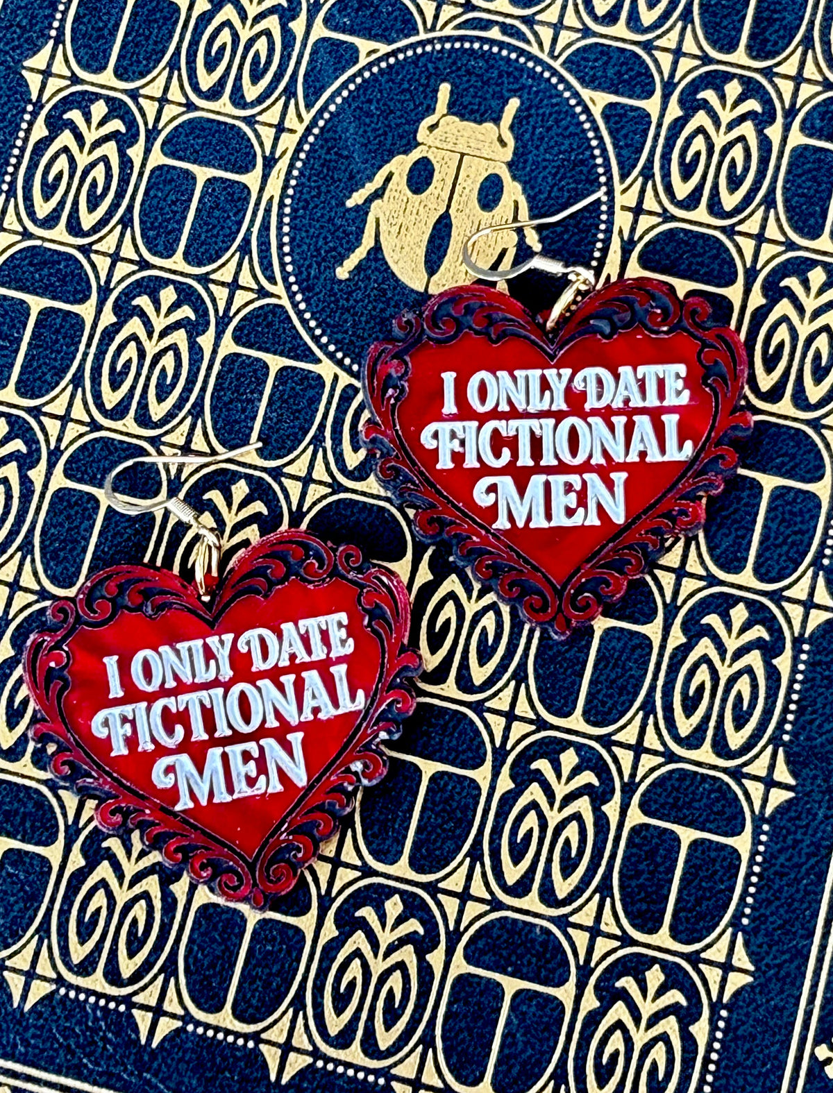 Red I Only Date Fictional Men romance reader earrings with ornate black heart details on a black and gold vintage book