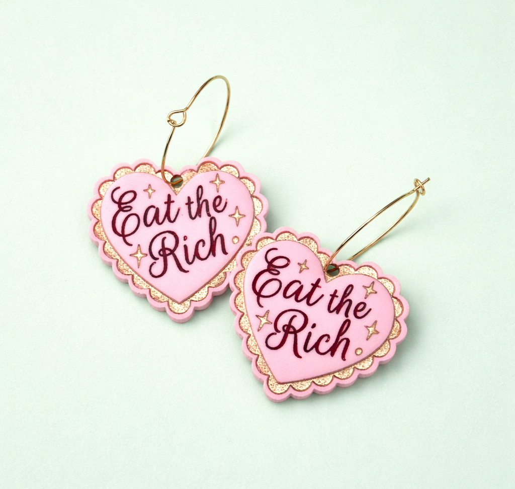 Pink earrings with 'Eat the Rich' text on a light green background
