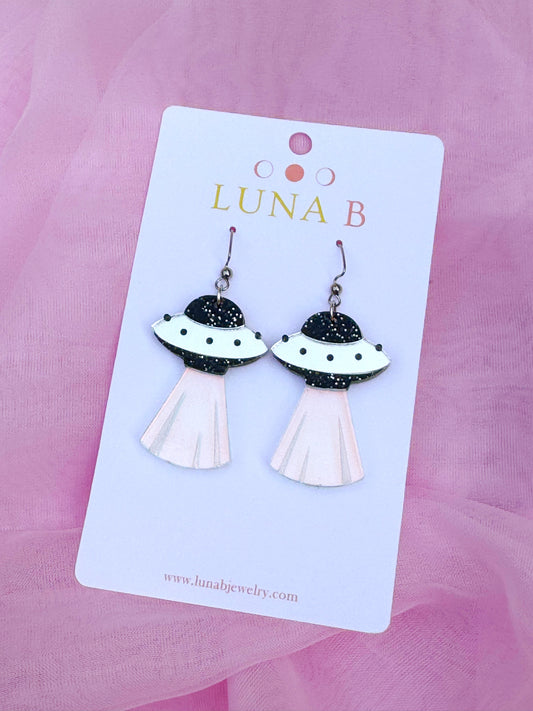 Flying saucer-shaped acrylic earrings with silver glitter and iridescent light beam, handmade with stainless steel ear wires.