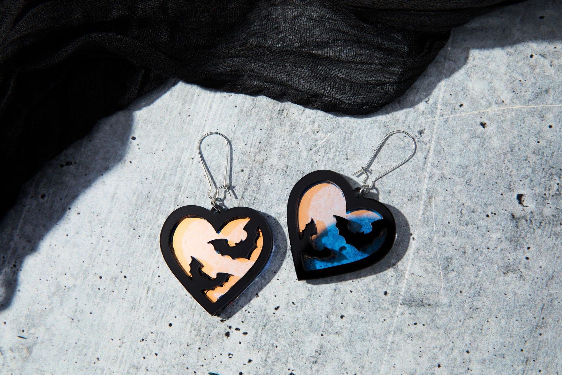Close-up of Freakin’ Bats earrings featuring black acrylic bats layered over an iridescent background, dangling from stainless steel kidney hooks.