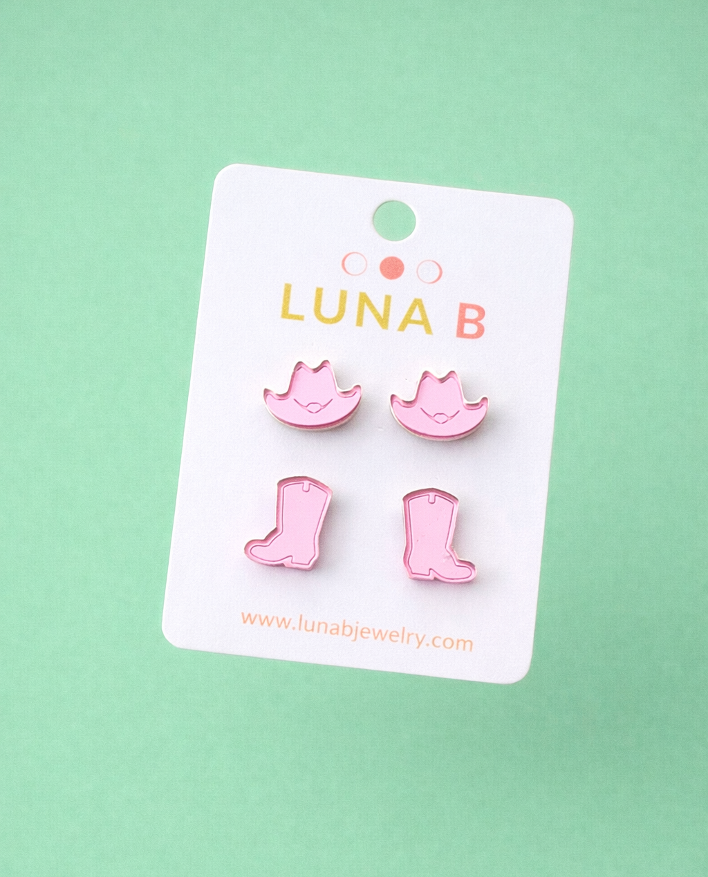 Pink boot-shaped earrings on a Luna B branded card against a light green background