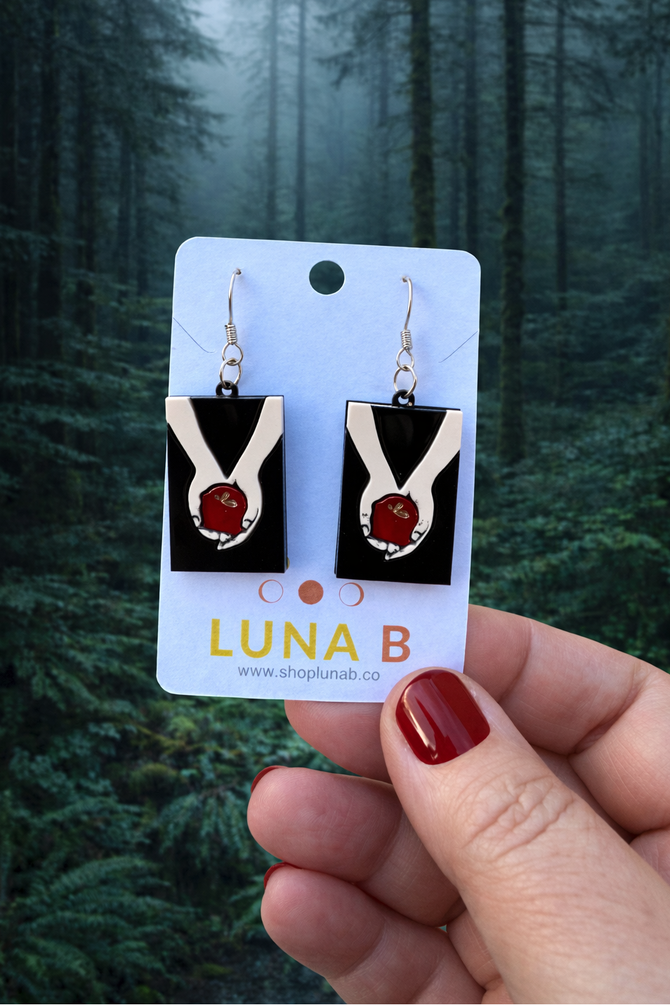 Earrings on a Luna B card held against a forest background
