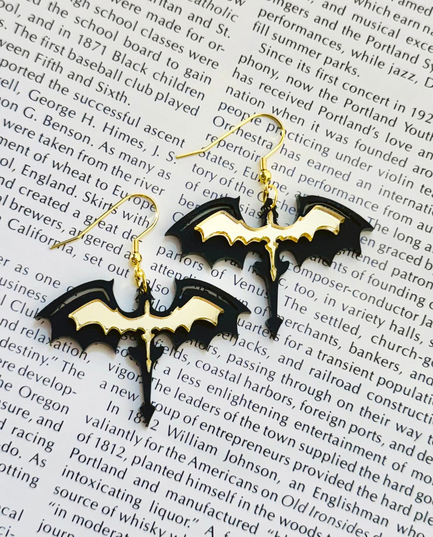 Black acrylic dragon silhouette earrings with gold detailing on stainless steel hooks, photographed on an open book page.