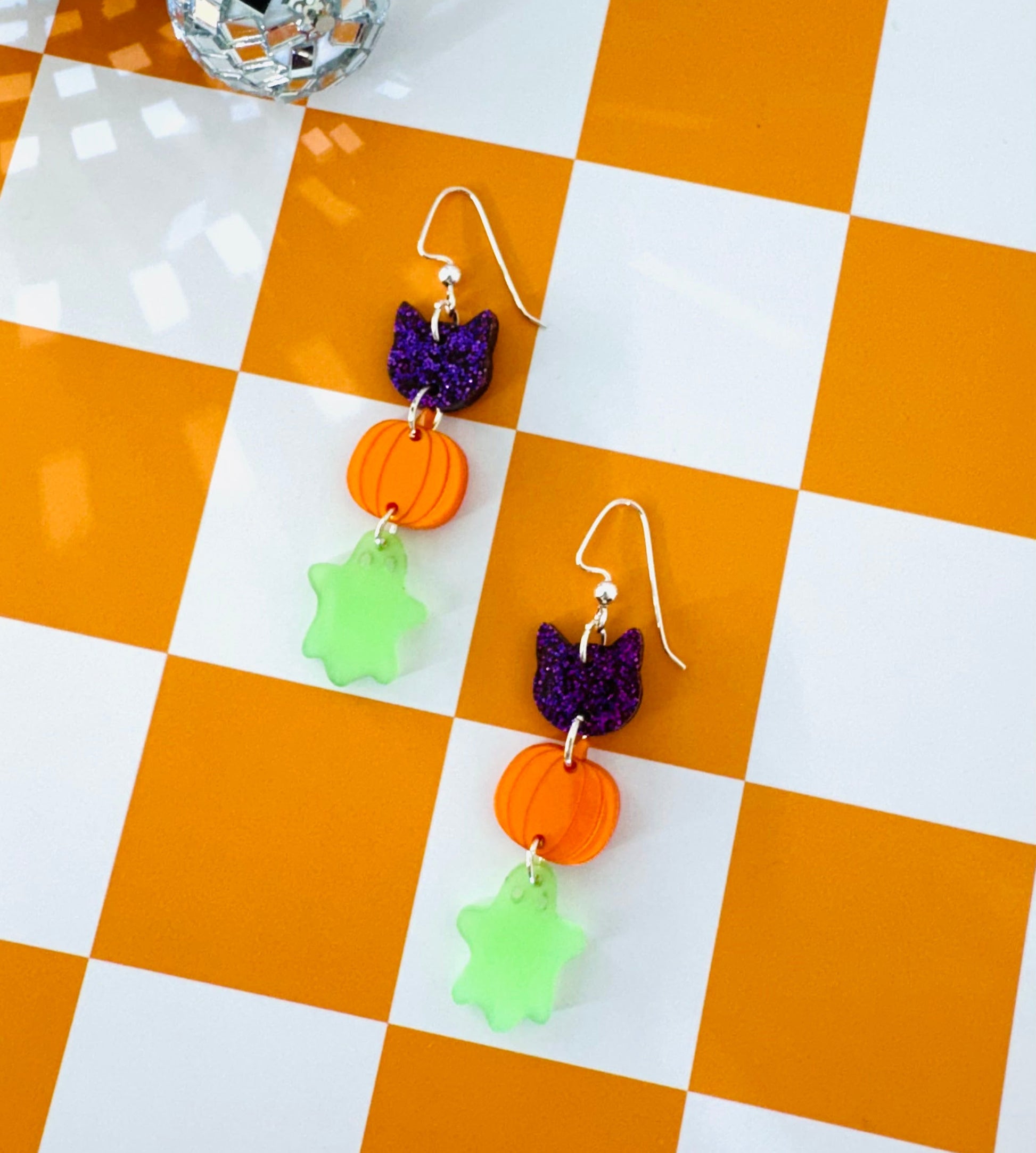 Pair of Halloween-themed earrings on a checkered orange and white surface.