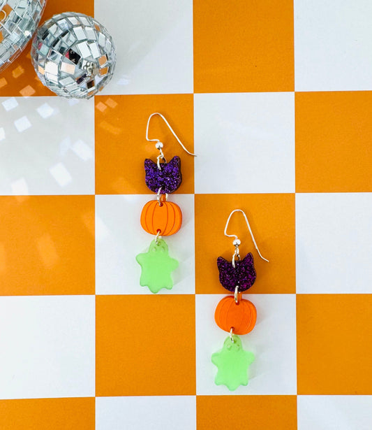Halloween-themed earrings on a checkered orange and white surface with a disco ball.