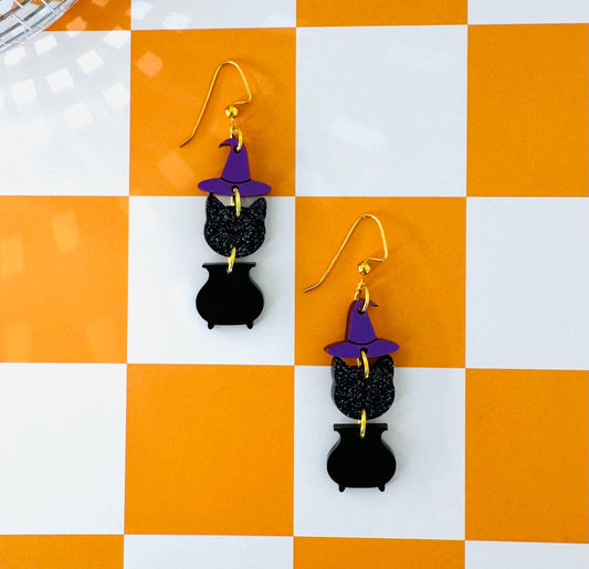 Black cat earrings with purple hats on a checkered orange and white background