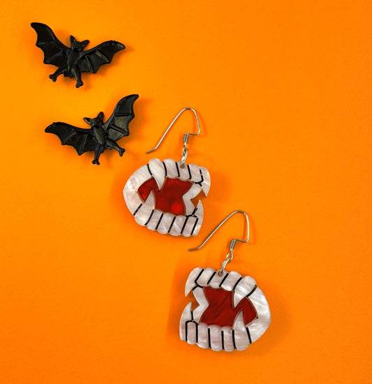 Halloween-themed earrings with black bats on an orange background