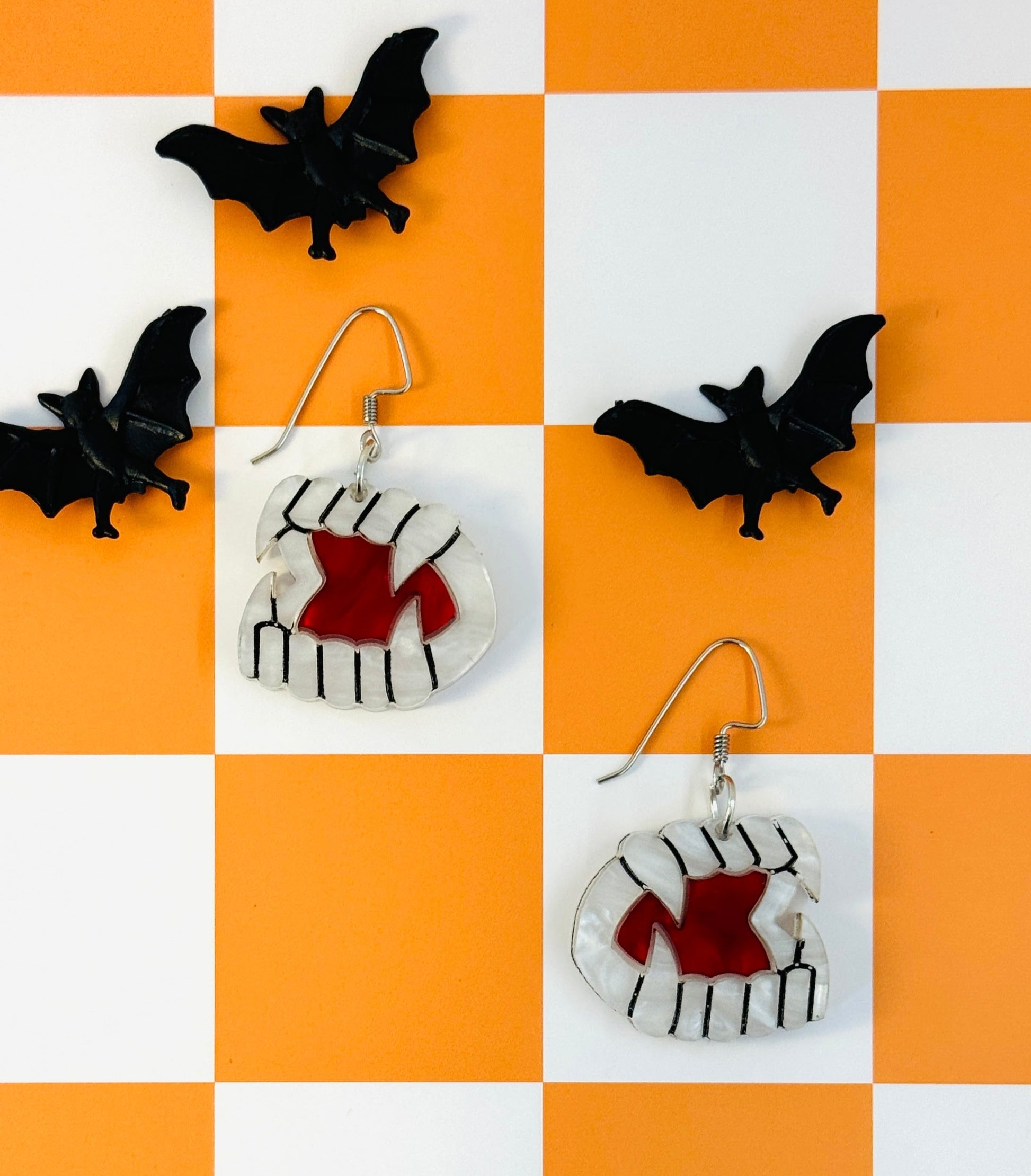 Halloween-themed earrings with bat designs on a checkered orange and white background.