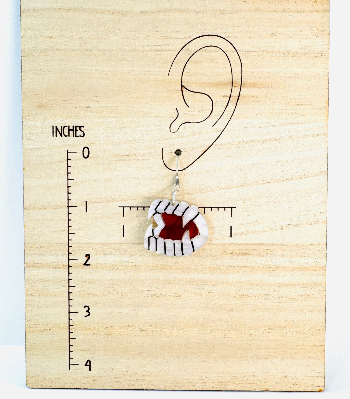 Earring on a wooden block with an ear illustration and measurement scale