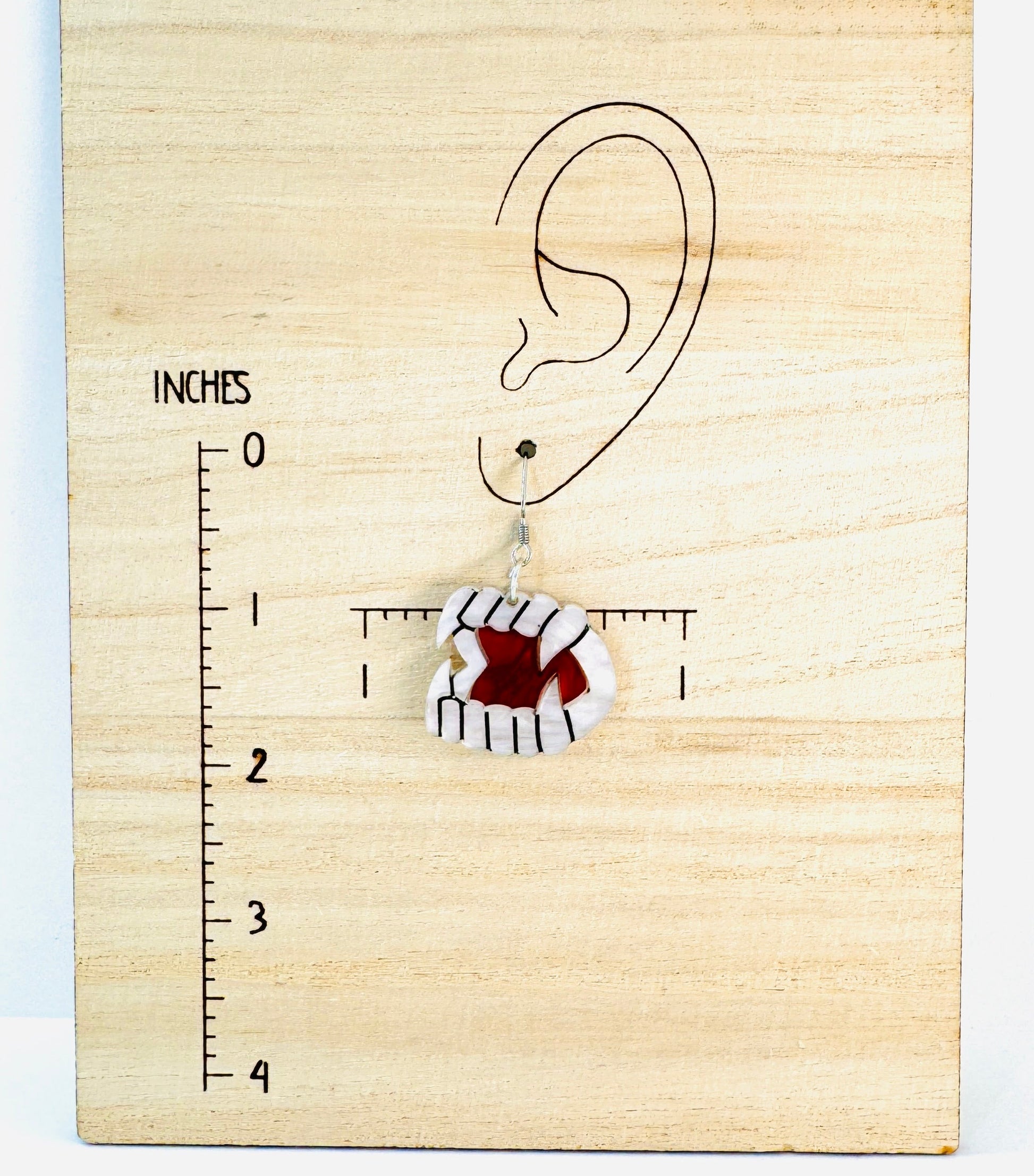 Earring on a wooden block with an ear illustration and measurement scale