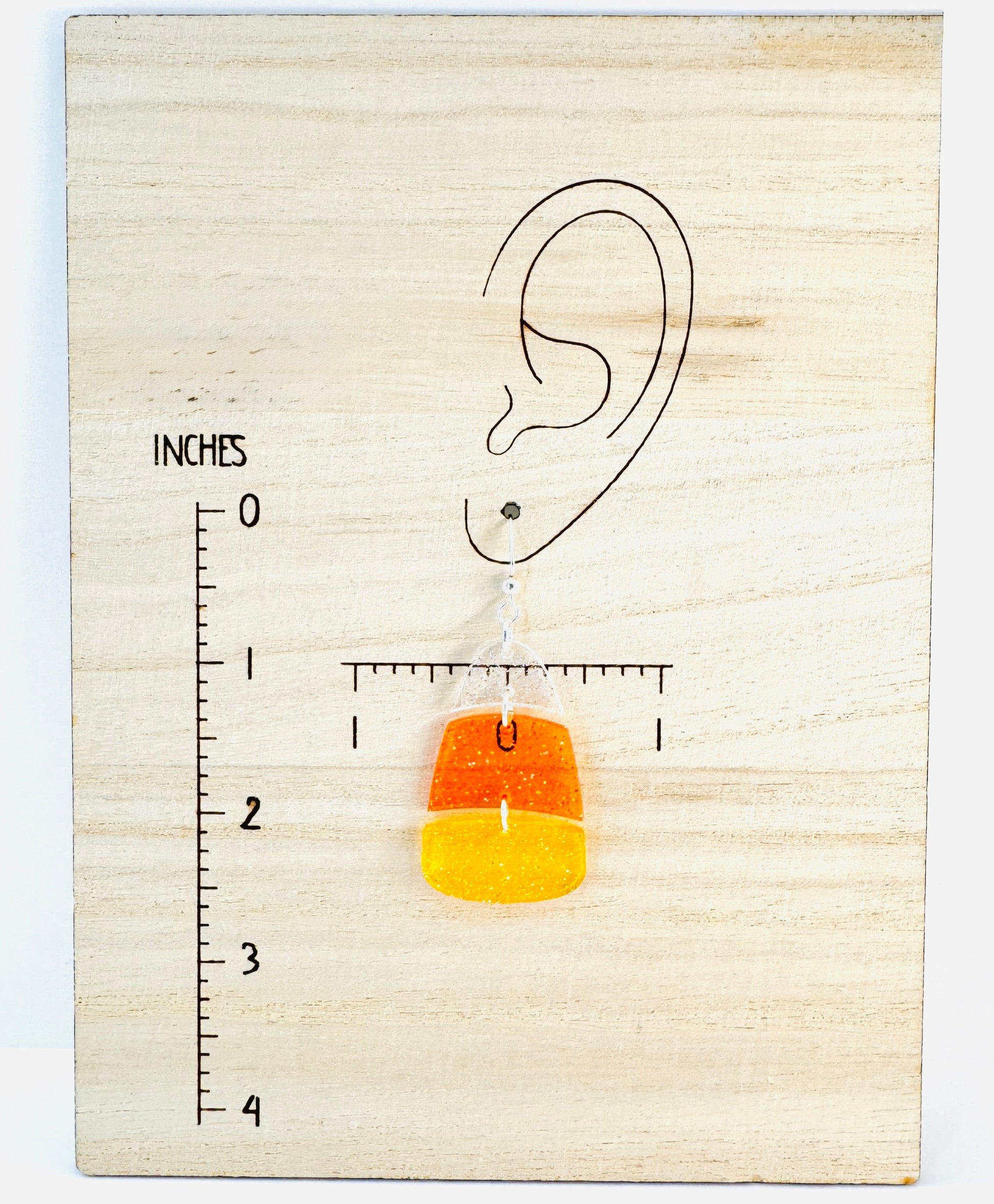 Earring displayed on a wooden block with an ear diagram and measurement scale.
