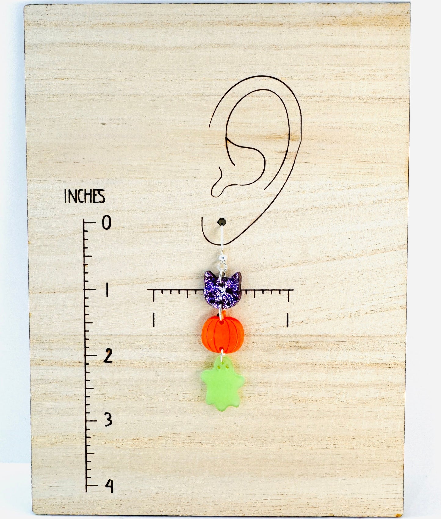 Earring displayed on a wooden block with an ear diagram and measurement scale.