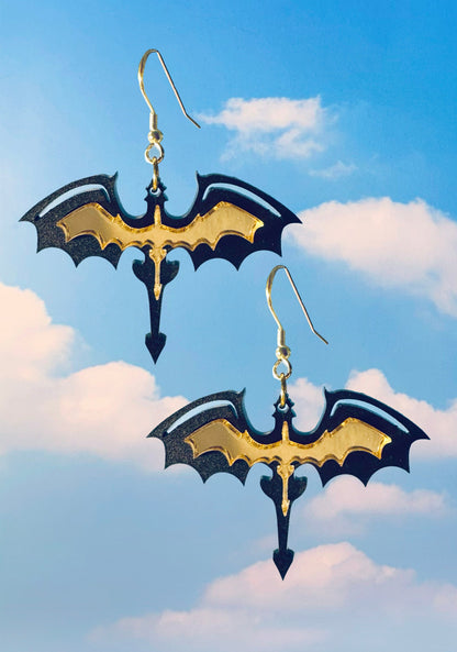 Black acrylic dragon silhouette earrings with gold detailing on gold hooks, photographed on an open blue sky with clouds.
