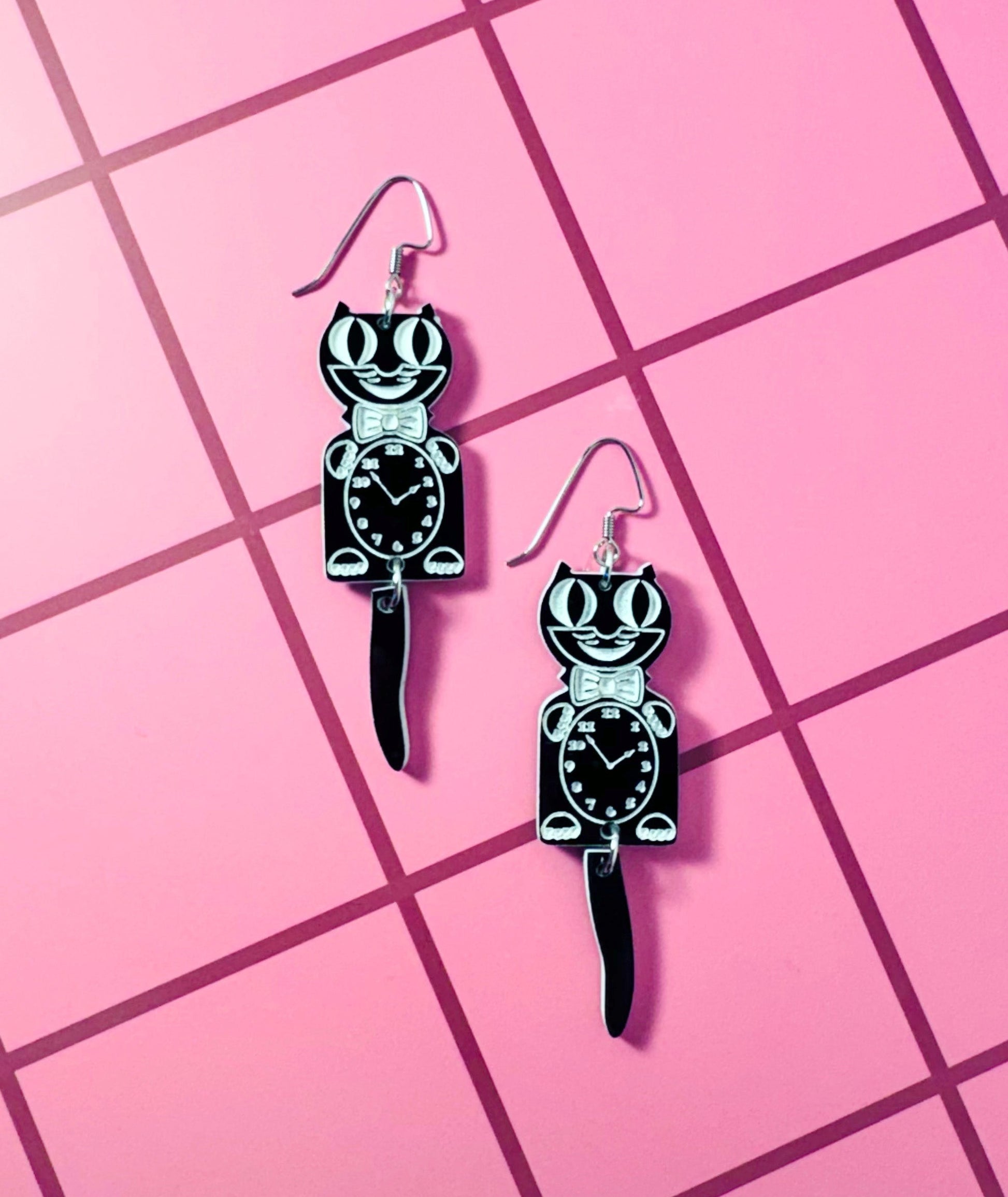 Pair of black and white cat-shaped earrings on a pink grid background