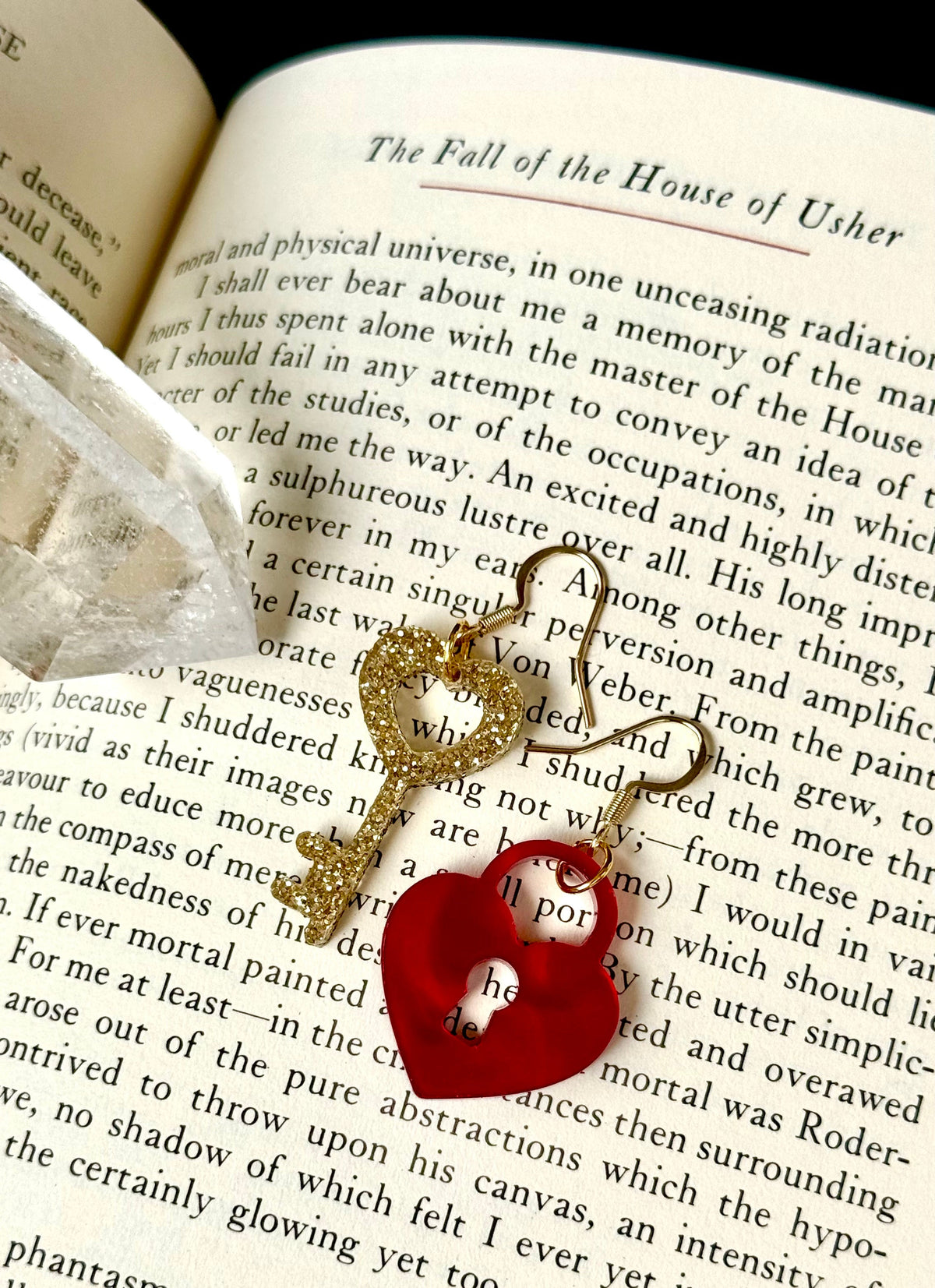 A gold-toned metal key with a red heart-shaped charm resting on open book pages.