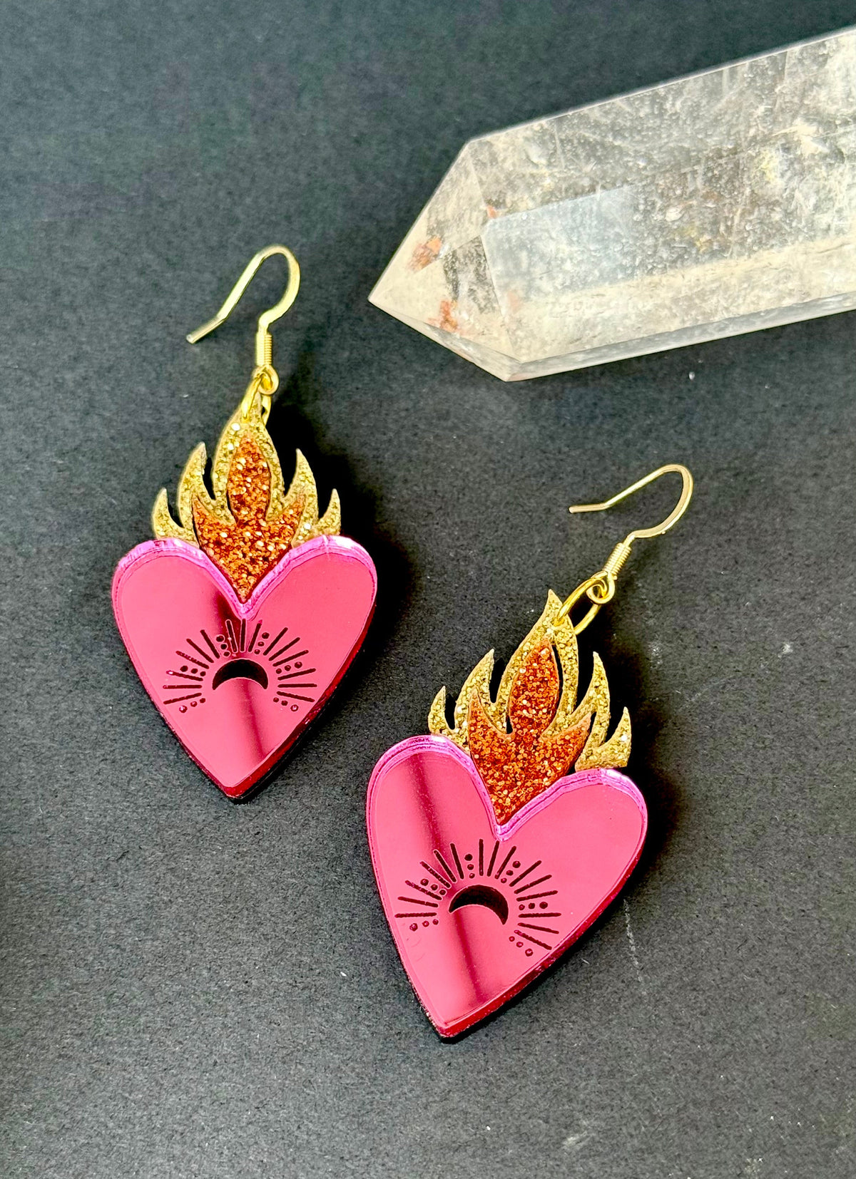 Pink mirrored flaming heart earrings with copper and gold glitter flames and crescent moon engraving beside a clear crystal