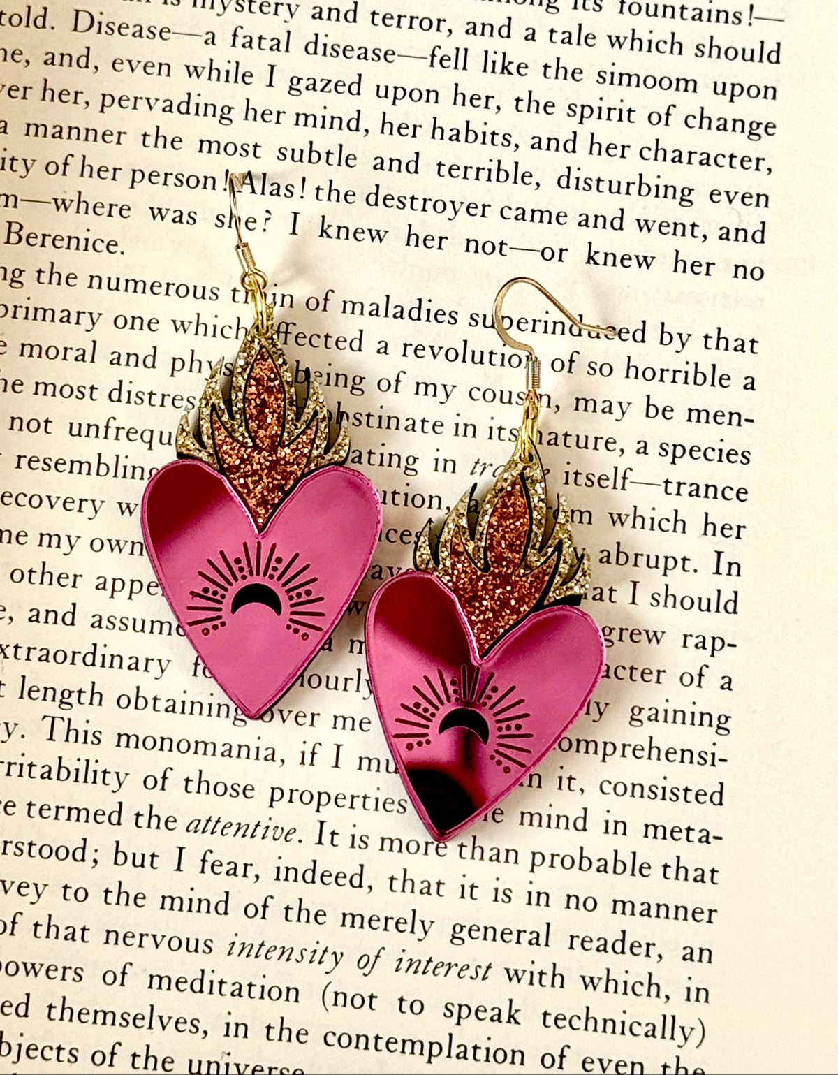 Handmade pink mirror flaming heart earrings with gold and copper glitter flames displayed on an open vintage book