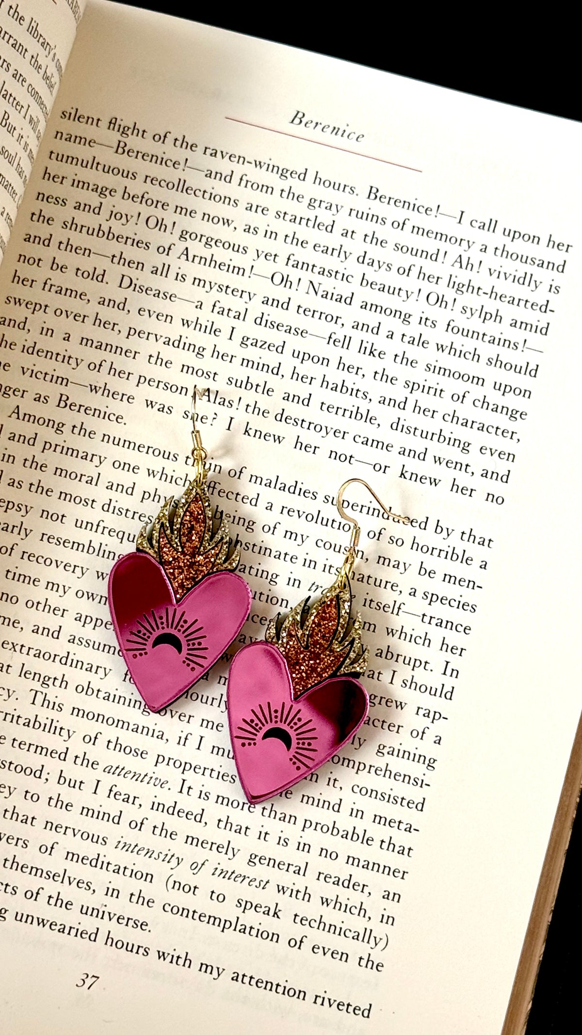 Handmade pink mirror flaming heart earrings with gold and copper glitter flames displayed on an open vintage book