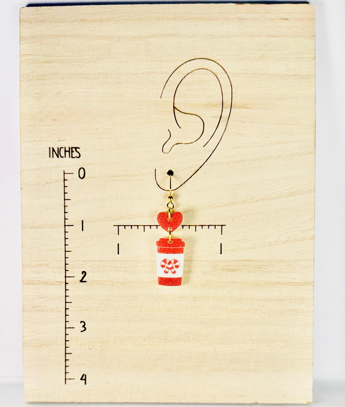 Earring with a cup and heart design on a wooden block with measurement scale