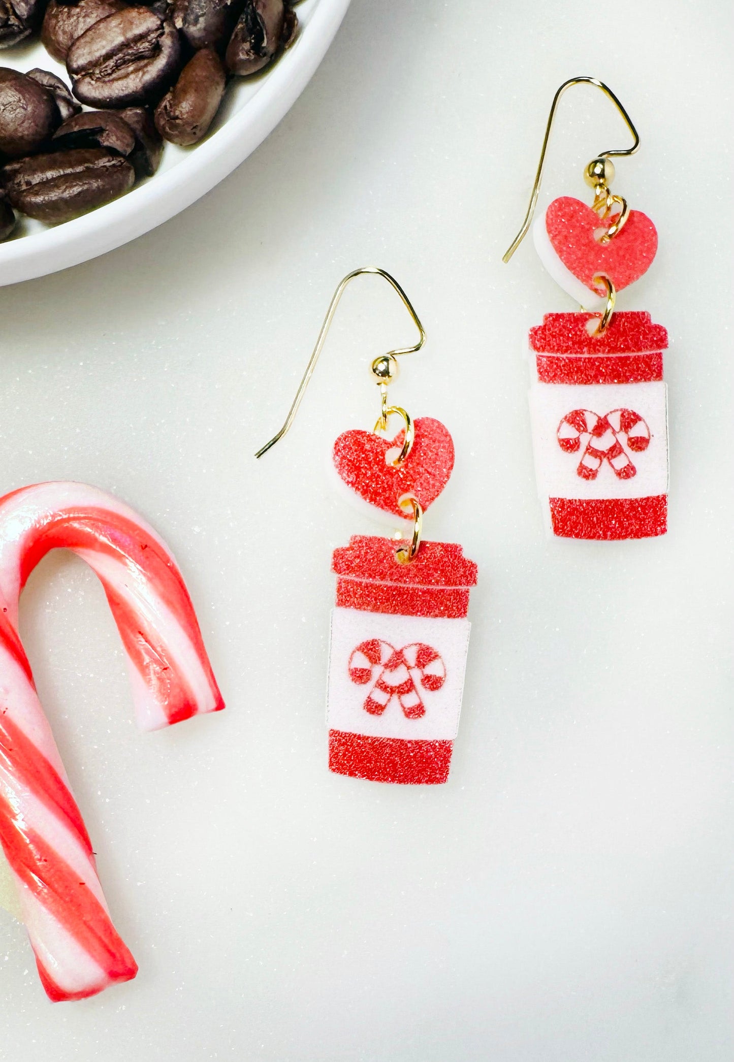 Pair of earrings resembling coffee cups with a candy cane on a white background