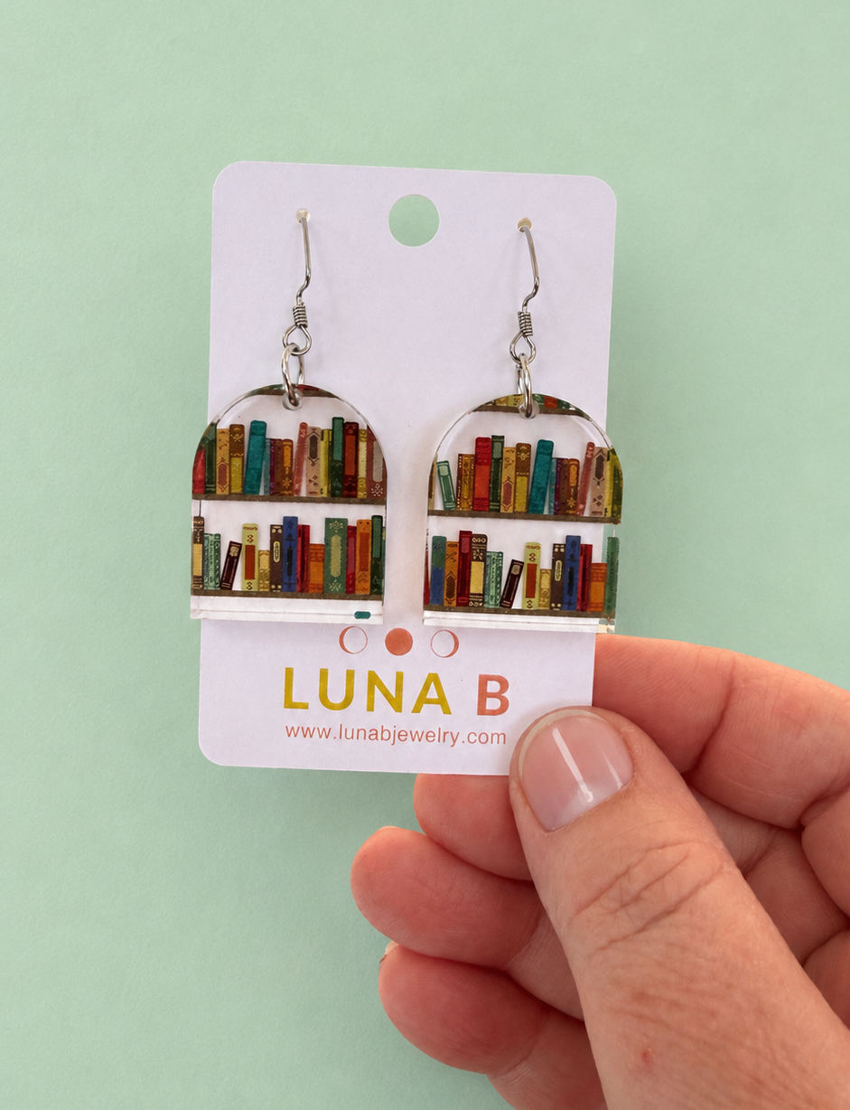 Earrings on a card held by a hand with a light green background