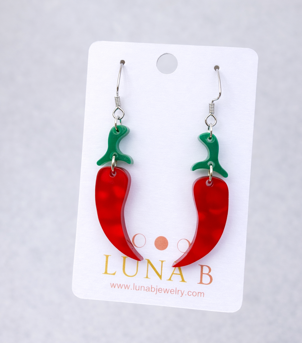 Handmade red chili pepper dangle earrings with green acrylic stems on stainless steel ear wires, photographed on a branded Luna B card.