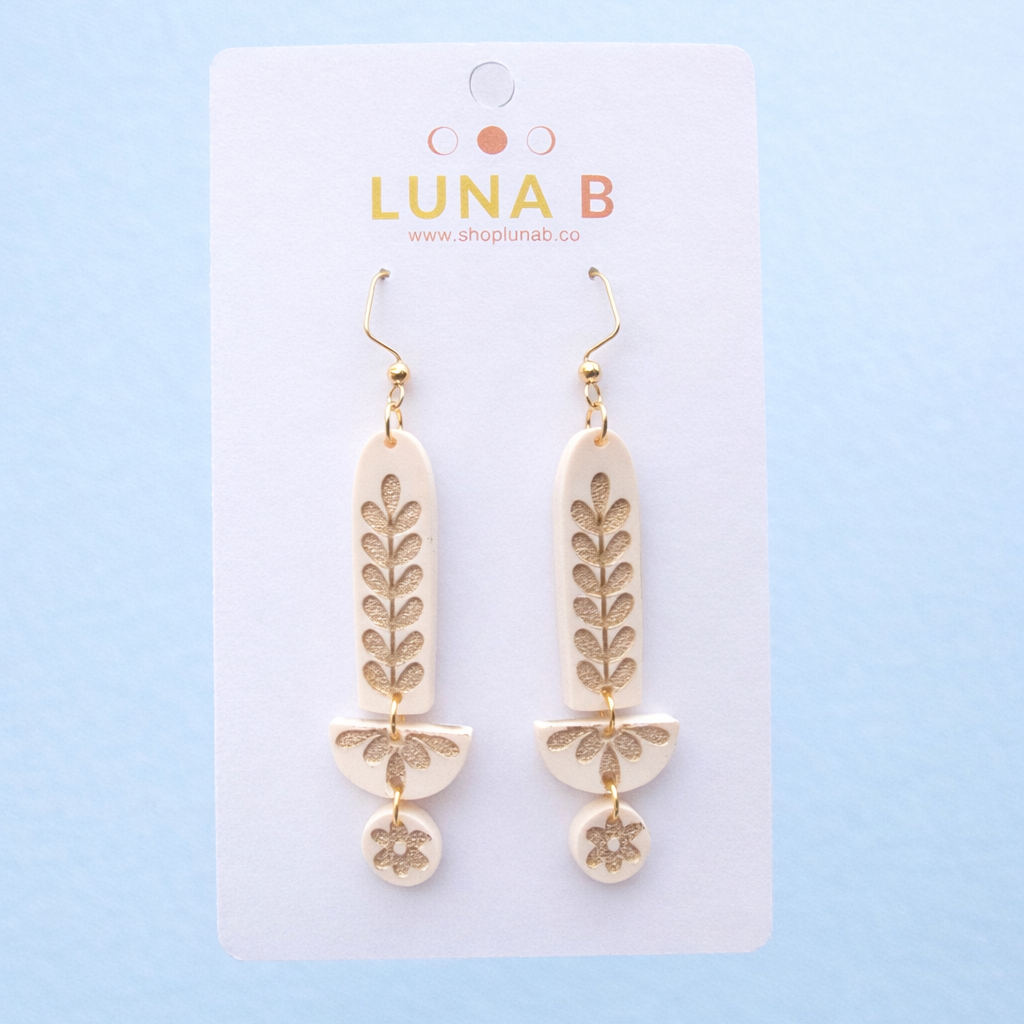 Cream and gold earrings on a Luna B branded card against a light blue background