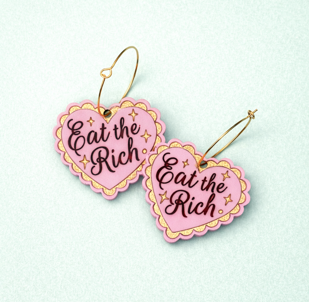 Heart-shaped earrings with 'Eat the Rich' text on a light blue background