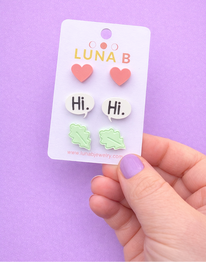 Card with heart-shaped earrings and 'Hi' speech bubbles held against a purple background