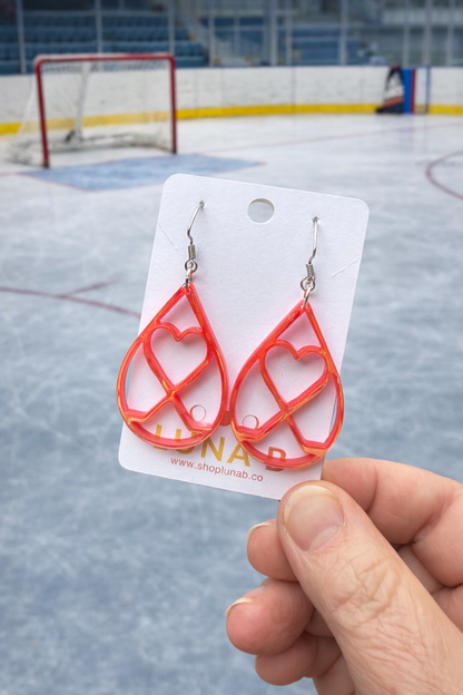 Red heart-shaped earrings on a white card held in front of an ice rink.