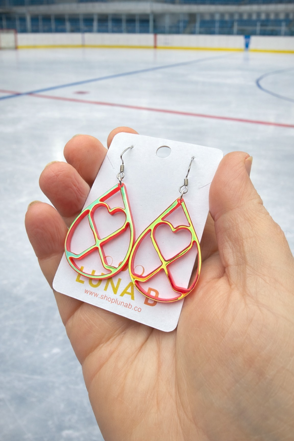 Heart-shaped earrings on a card held in front of an ice rink.