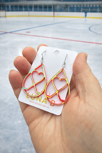 Heart-shaped earrings on a card held in front of an ice rink.