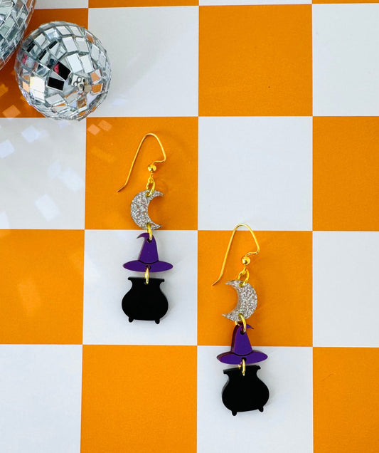 Pair of earrings with black cat and witch hat design on a checkered orange and white background.