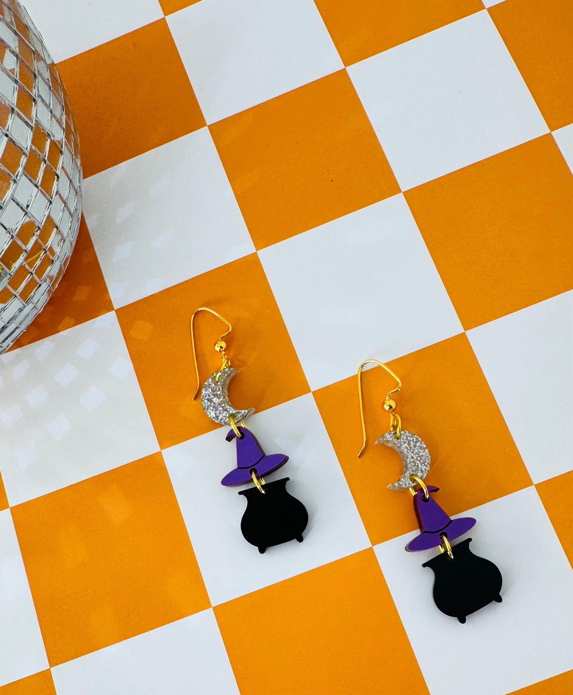 Pair of witch-themed earrings on a checkered orange and white surface