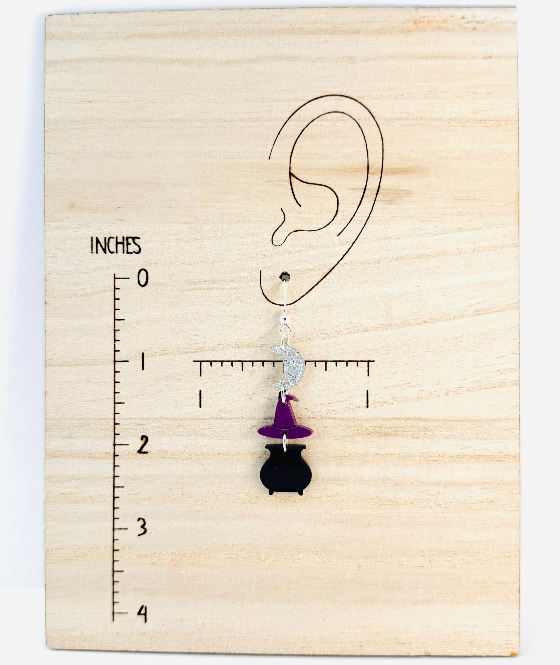 Earring displayed on a wooden block with an ear illustration and measurement scale.