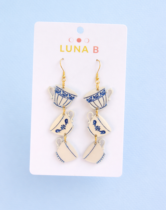 Stacked teacup dangle earrings with blue floral pattern on white acrylic, displayed on a white card
