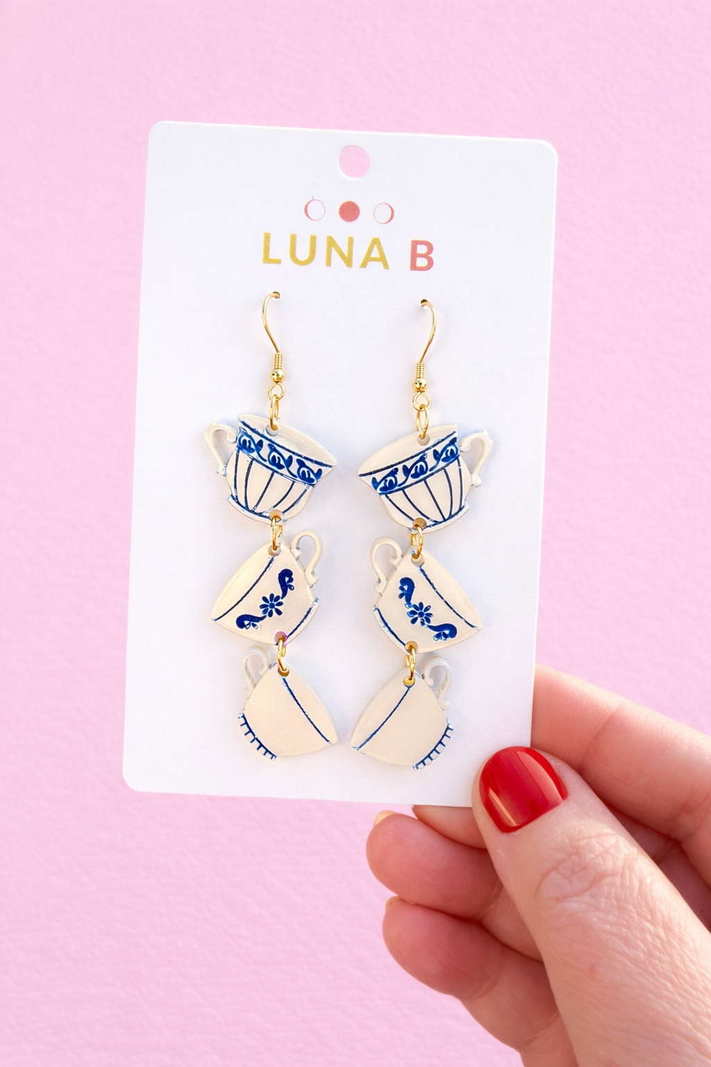 Stacked teacup dangle earrings with blue floral pattern on white acrylic, displayed on a white card